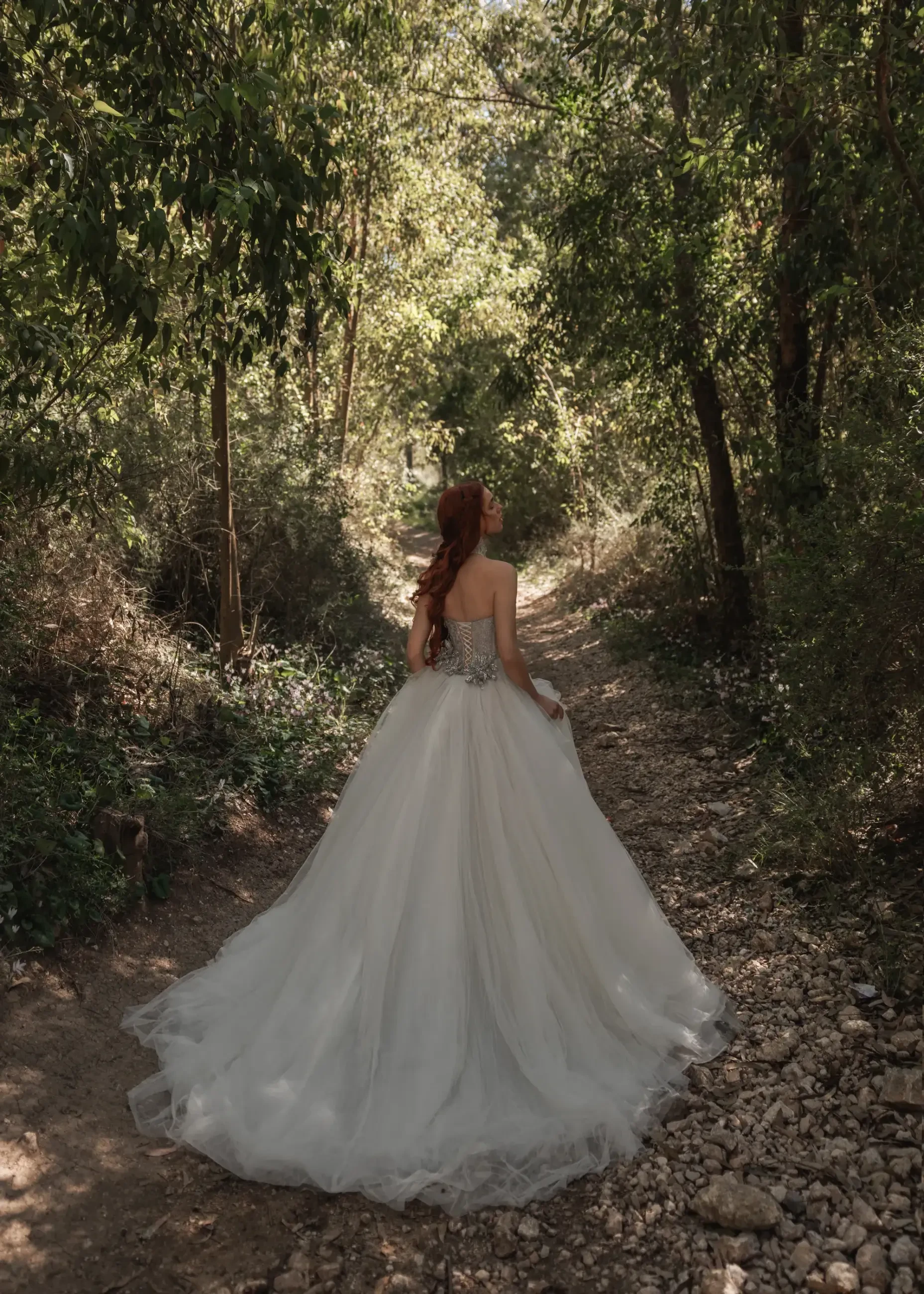 A woman in a flowing white wedding dress walks through a sun-dappled forest path, surrounded by lush greenery, conveying a serene, romantic mood.