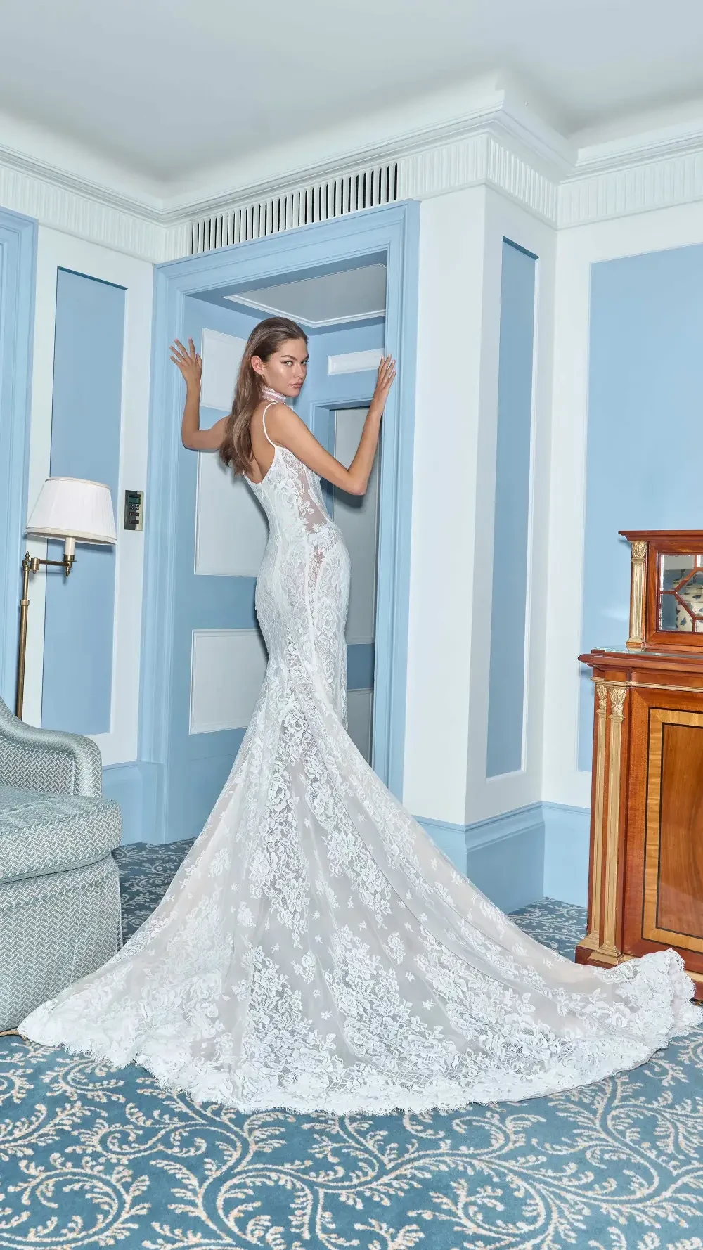 A woman in a white lace wedding dress standing by a door in a decorated room.