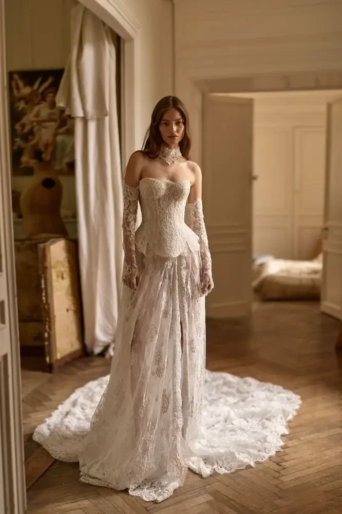 A woman in a white wedding dress stands in a softly lit room with elegant decor.